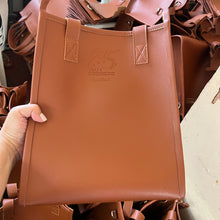 Load image into Gallery viewer, Brown leather handbag held by a person with a blurred background
